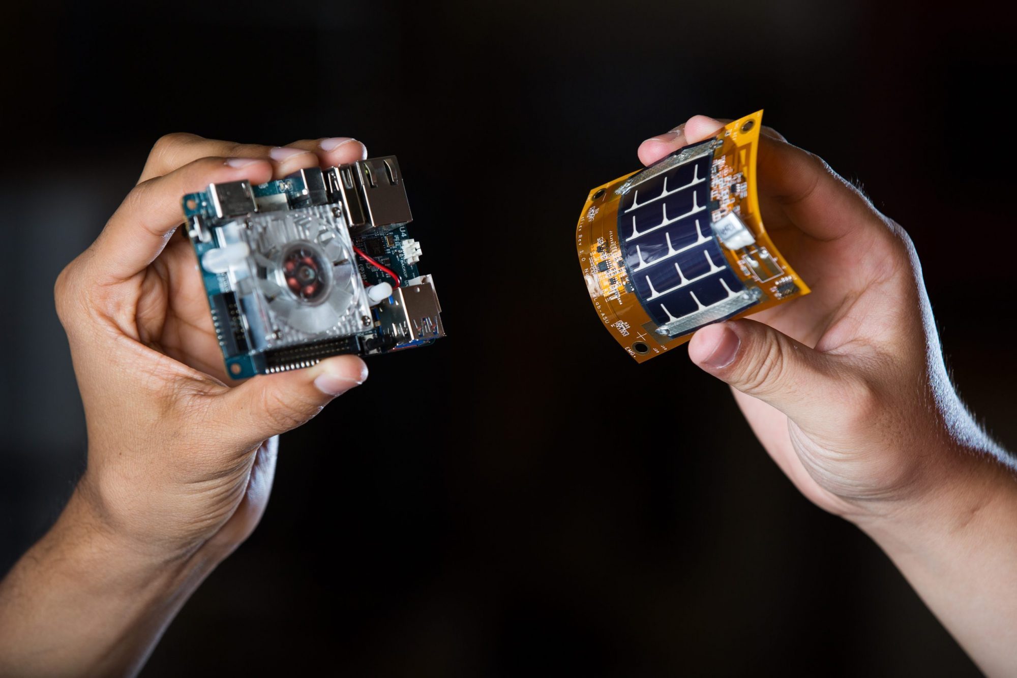 Two hands holding small electronic components against a dark background